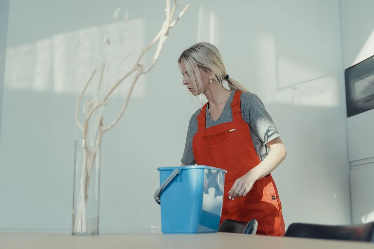 A uniformed cleaner with a bucket working in a bright commercial space