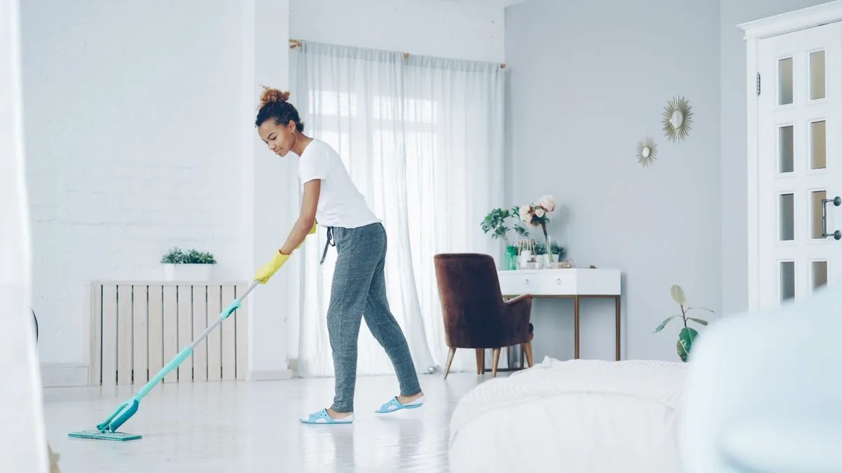 A woman mopping the floor of a bright, empty apartment