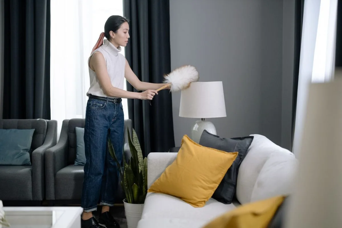 A woman dusting a lampshade in a bright modern living room